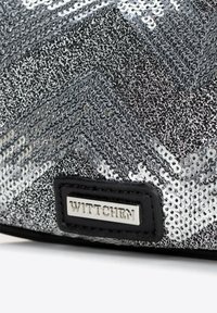 Borsa a tracolla in paillettes argentate con motivo zigzag, dettagli neri e superficie testurizzata. Etichetta del marchio "WITTCHEN" attaccata.