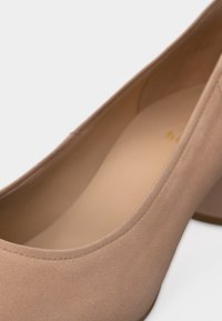 Γόβα σε μπεζ σουέντ με ψηλό τακούνι, παρουσιάζοντας στρογγυλεμένη μύτη, ομαλές ραφές και επενδεδυμένο πέλμα σε λευκό φόντο.