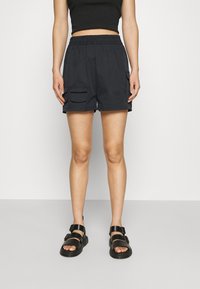 Svarta cargoshorts med elastisk midja, två sidofickor och en avslappnad passform, kombinerade med svarta sandaler med spännband.