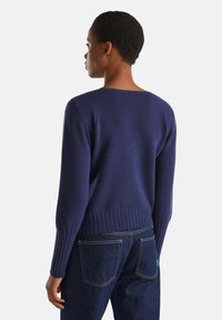 Marineblauer Strickpullover mit lockerer Passform, gerippten Bündchen und Saum. Verfügt über einen weiten Ausschnitt und eine weiche Textur. Kombiniert mit blauen Jeans.