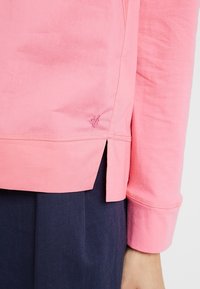 Top a maniche lunghe rosa con uno spacco laterale, caratterizzato da un piccolo logo ricamato vicino all'orlo, realizzato in tessuto morbido e con vestibilità comoda.