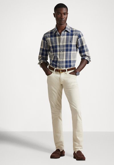 Καρό πουκάμισο με κουμπιά σε ναυτικό μπλε, κρεμ και μπλε; κρεμ chino παντελόνι; καφέ ζώνη; καφέ μοκασίνια; κοντά μανίκια σηκωμένα.