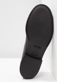 Suola di calzature nera con motivo testurizzato e bordi arrotondati. Presenta il nome del marchio "Camper" inciso e un logo vicino al tallone.