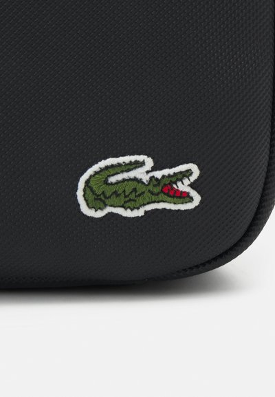 Sac en matériau texturé noir avec un logo crocodile brodé vert et rouge, souligné de blanc, placé sur le devant.