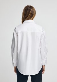 Witte langarmige shirt met een knoopsluiting kraag, met een effen textuur, een rugplooi detail en knoopmanchetten.