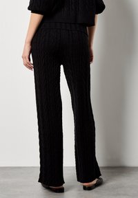 Zwarte kabelgebreide broek met een uitlopende snit, voorzien van een textuurpatroon. De stof heeft een zachte uitstraling, die een minimalistische stijl aanvult.