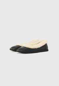 Scarpe slip-on nere con un morbido colletto in ecopelliccia color crema. Realizzate in pelle, dotate di suola piatta e logo cucito sul lato.