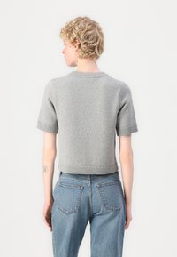 Hellgrauer, kurzärmeliger Strickpullover mit geripptem Saum und Halsausschnitt, der eine körpernahe Passform und eine glatte Textur aufweist. Dazu werden blaue Jeans getragen.