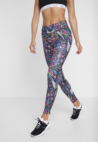 Leggings coloridos con patrones florales y geométricos, que cuentan con una cintura alta, tejido elástico y acentos negros, combinados con zapatillas deportivas.
