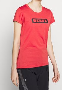 Red cotton t-shirt with a rounded neckline and short sleeves. Features a black logo across the chest. Smooth texture, casual design.