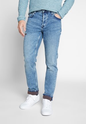 Helle blaue Jeans im Slim-Fit mit klassischem Fünf-Taschen-Design, hochgekrempelten Säumen und dezenten Ausbleichungen. Kombiniert mit weißen Sneakern.