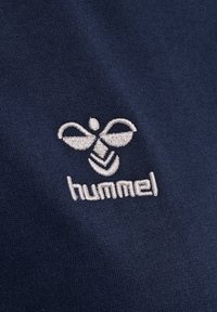 Mörkblått tyg med slät yta; har en ljusgrå broderad logotyp av en bi och ordet "hummel" under.