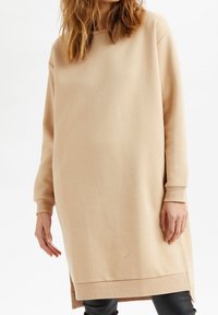 Beige sweatshirtklänning med långa ärmar, rund halsringning och sidsprund. Tillverkad av mjukt material och har en avslappnad, löst sittande design.