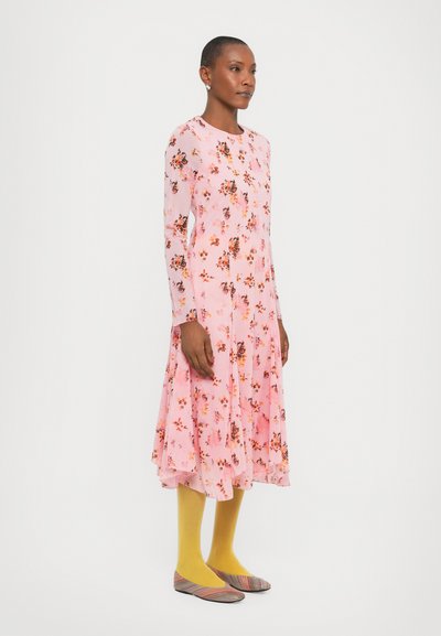 Langarmige roze jurk met bloemenprint, flaired silhouet, gecombineerd met gele kousen en kleurrijke platte schoenen; gladde textuur.