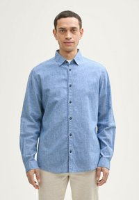 Knoopshirt in lichtblauwe stof met een gestructureerde afwerking, lange mouwen en donkere knopen aan de voorkant. Eenvoudig kraagontwerp.