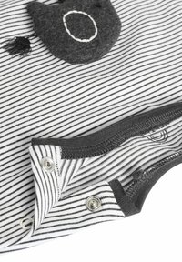 Zwart-wit gestreepte jumpsuit met een grijze kattenvormige zak, metalen drukknoopjes en een zachte katoenen stof. Soepele textuur met contrasterende accenten.
