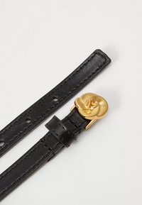Zwarte leren riem met een gladde textuur, voorzien van een gouden bloemvormige gesp en meerdere verstelgaatjes.