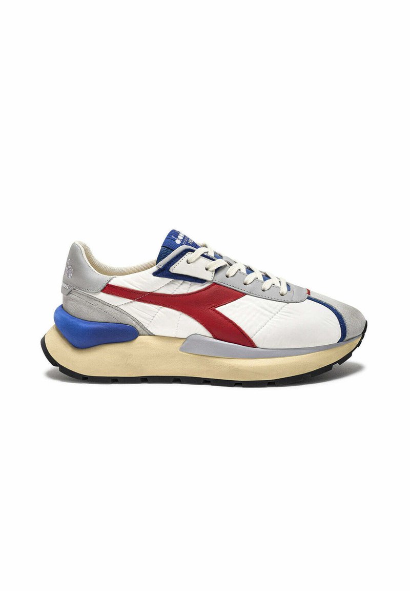 Sneakers bianchi con accenti rossi e blu, dotati di una tomaia testurizzata, sovrapposizioni grigie e una suola chunky beige. I lacci sono di un grigio chiaro.