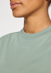 Mint green cotton t-shirt with a round neckline and subtle "BORG" logo printed in the same color on the chest. Smooth texture.