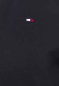 Granatowy sweter z dzianiny z małym, haftowanym logo w kolorach czerwonym, białym i niebieskim po lewej stronie. Gładka tekstura z dopasowanym krojem.