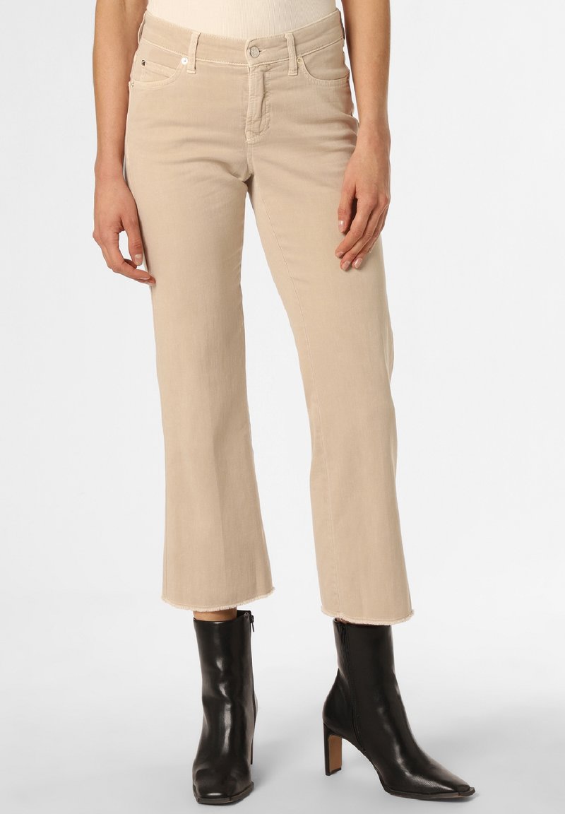 Jeans beige acampanados con un dobladillo sin acabar, bolsillos frontales y una cintura ajustada, combinados con botas negras de tobillo con tacón cuadrado.