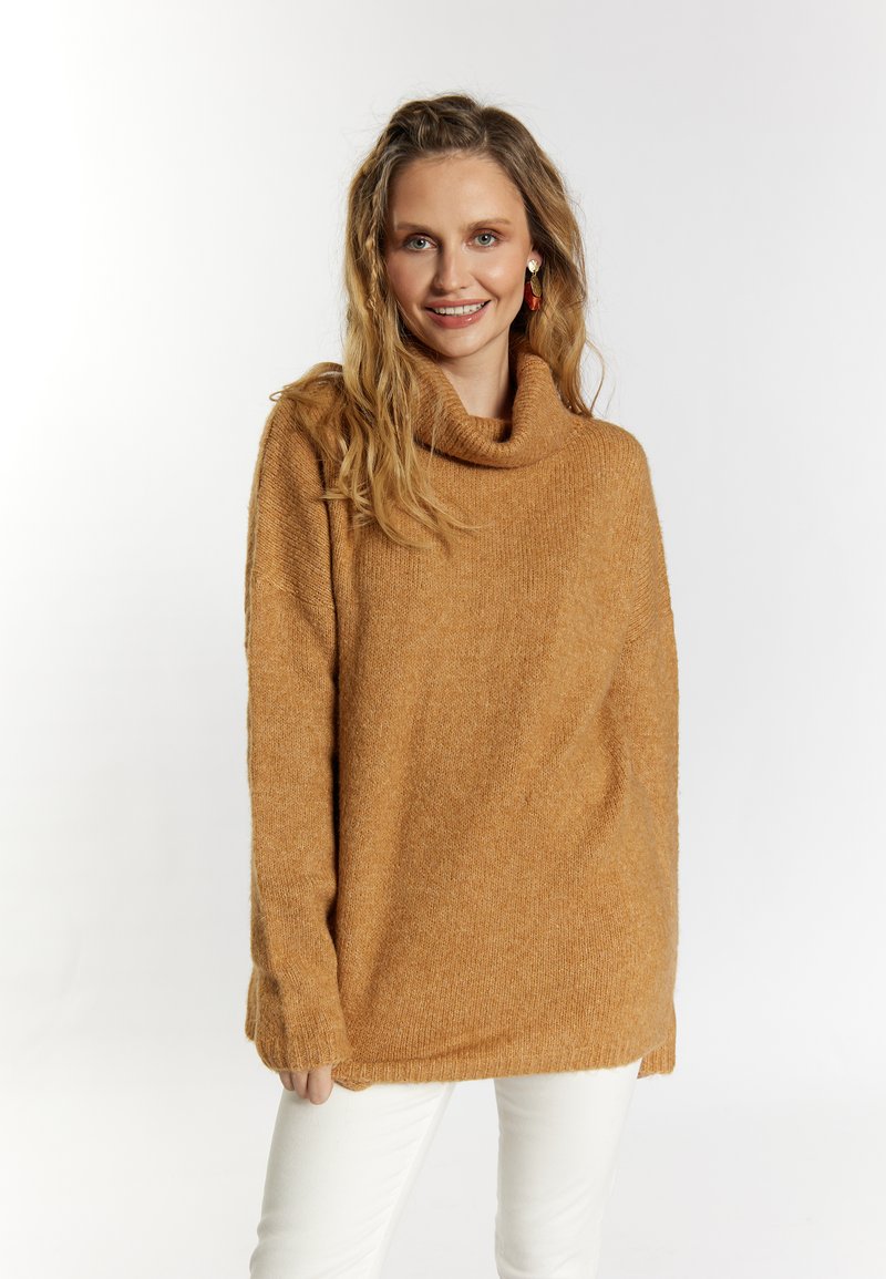 Pulover texturat de culoare muștar, cu guler tip cowl și mâneci lungi, asociat cu pantaloni albi. Are croială lejeră și fanteze subtile.