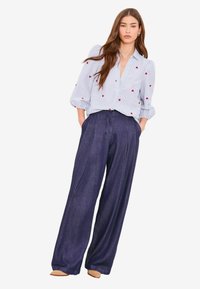 Gestreifte hellblaue Bluse mit roter Herzstickerei, kombiniert mit hochtaillierter, weit geschnittener dunkler Denim-Hose. Glatte Textur, lässige Passform.