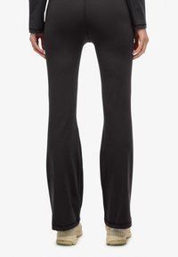 Czarne legginsy o rozszerzanym kroju, wykonane z elastycznego materiału. Gładka tekstura, bez widocznych wzorów, w połączeniu z beżowymi trampkami.