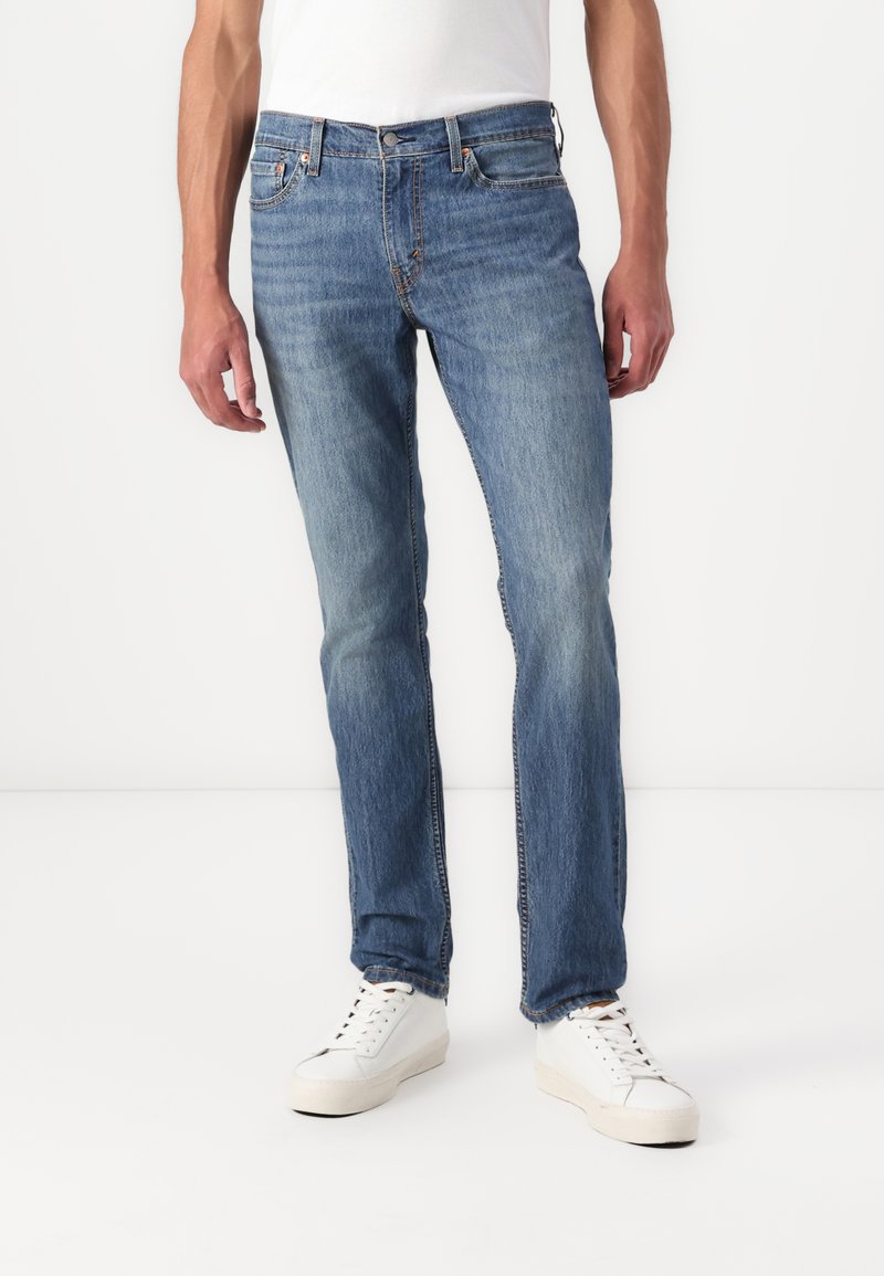 Jeans de mezclilla en un tono azul claro con corte recto, diseño de cinco bolsillos y costuras en contraste. Llevados con zapatillas blancas sobre un fondo neutro.