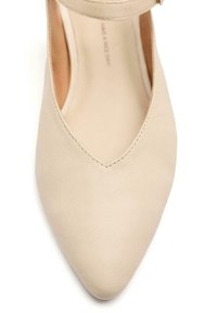 Scarpa in pelle beige con punta affusolata e cinturino alla caviglia. Texture liscia con una leggera lucentezza, che mette in mostra un design minimalista.