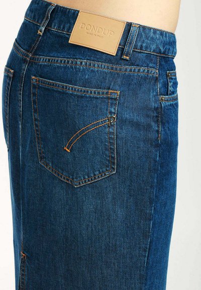 Jeans de denim en azul oscuro con costuras naranjas. Presentan una etiqueta de cuero en la cinturilla y un bolsillo trasero con un detalle de costura en curva.