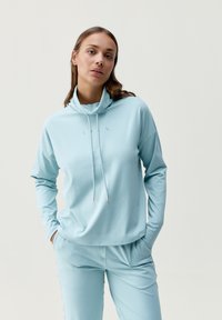 Suéter azul claro de manga larga con cuello alto, cordón y textura suave, combinado con pantalones azul claro a juego.