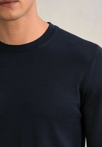 Maglietta a manica lunga di colore blu navy con scollatura rotonda, texture a coste e dettagli cuciti lungo le cuciture. Realizzata in materiale morbido.