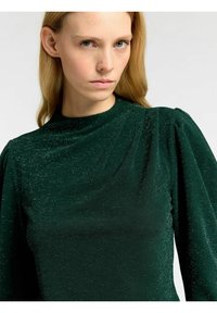 Grön glittrig topp med långa ärmar, hög hals och rynkdetalj på axlarna. Slät textur med en skimrande finish.