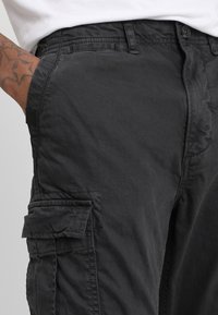 Zwarte cargobroek van stevig materiaal, met meerdere zijzakken, een ontspannen pasvorm en zichtbare stikseldetails.