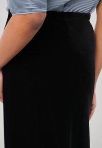 Schwarzer Samtrock mit einer figurbetonten Silhouette, der eine glatte Textur und eine Seitennaht aufweist. Das Design hebt einen schlanken, minimalistischen Stil hervor.