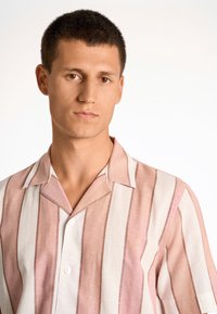 Camicetta a maniche corte in lino a righe rosa chiaro e bianche, con colletto a punte e chiusura a un bottone. Tessuto morbido, vestibilità rilassata.