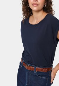 Tumši zila īsām piedurknēm T-kreklu ar noapaļotu kakla izgriezumu, apvienots ar tumši zilu džinsa svārku un brūnu teksturētu jostu.