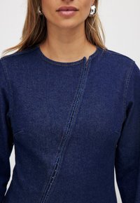 Džinsu kleita ar apaļu kakla izgriezumu, ar rāvējslēdzēju detaļu sānos un kontrastējošām šuvēm. Tumši zilā krāsā ar gludu tekstūru.