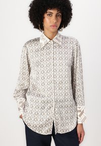 Light beige long-sleeve shirt with a geometric brown pattern. Features a contrasting patterned collar and cuffs, and button-down front.