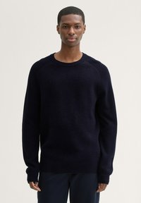 Pulover bleumarin cu o finisare texturată, guler rotund, manșete cu rigle și o croială lejeră. Materialul pare moale și călduros, potrivit pentru ținute casual.