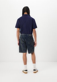 Camisa de manga corta en color navy combinada con pantalones cortos de mezclilla azul deslavado. El diseño presenta un cuello abotonado y bolsillos de parche en los pantalones cortos. Zapatos en blanco y negro.