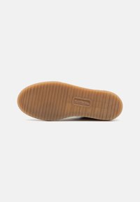 Semelle de chaussure en caoutchouc avec un motif texturé et nervuré. Couleur marron clair avec un bout rond et un détail de logo central.