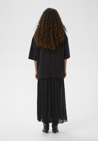 Schwarzes, übergroßes T-Shirt mit kurzen, weiten Ärmeln, kombiniert mit einem langen, durchsichtigen schwarzen Rock und spitzen schwarzen Stiefeletten.