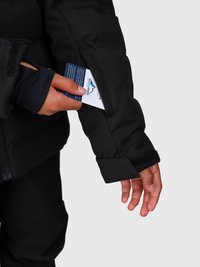 Rankomis dedama mėlyna ir balta kortelė į užtrauktuku uždaromą kišenę juodos striukės rankovėje prieš paprastą foną.