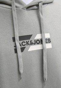 Sudadera gris hecha de una tela suave, que presenta un logotipo en blanco y negro audaz con acentos geométricos y cordones.