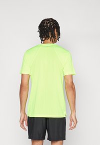 Neon zöld sportpóló rövid ujjakkal, struktúrált anyagból, kerek nyakkivágással és oldalsó hasítékokkal, fekete sorttal párosítva.