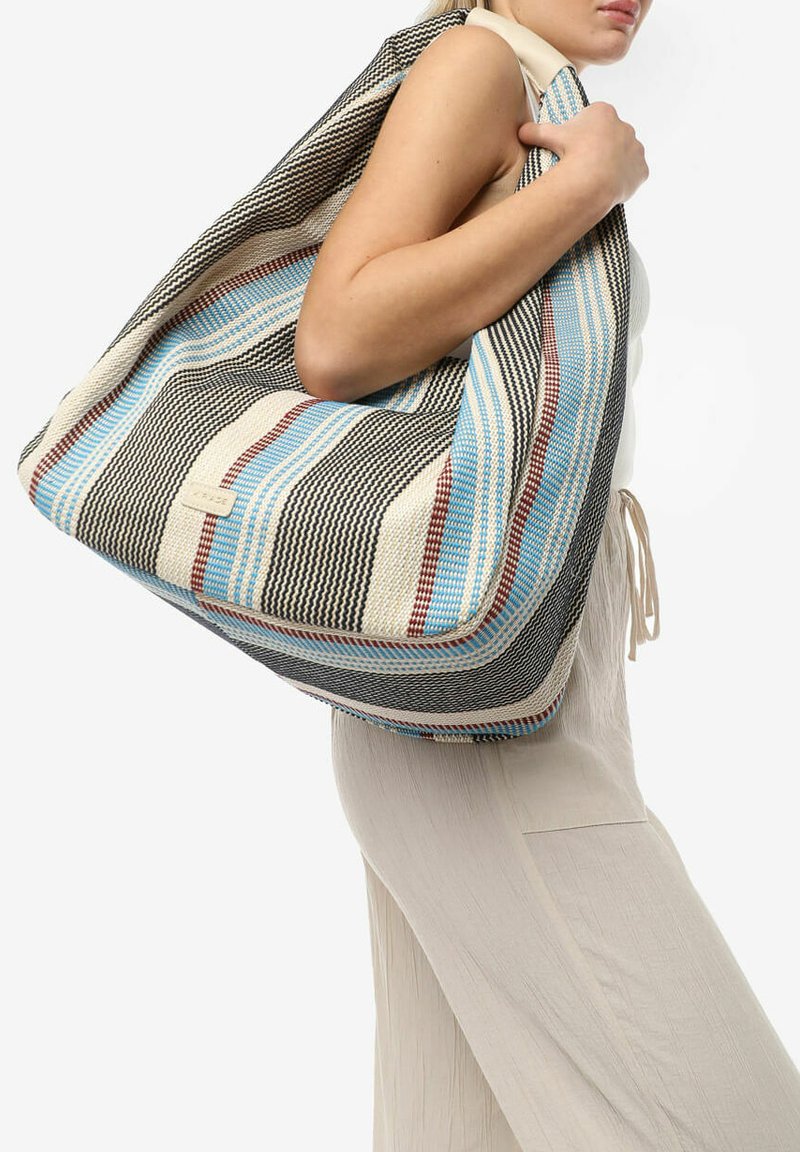 Stor vævet totebag med et stribet mønster i beige, blå og rød. Den har en blød tekstur og et rummeligt design, bæres over skulderen.
