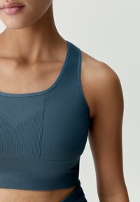 Mörk teal sportbh med ribbat mönster, en åtsittande design och ett geometriskt mönster fram. Breda axelremmar för stöd.