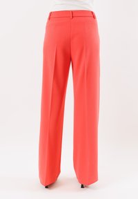 Pantaloni larghi corallo realizzati in un tessuto liscio, con vita alta, dettaglio plissettato sulla parte anteriore e sottili finiture sartoriali.